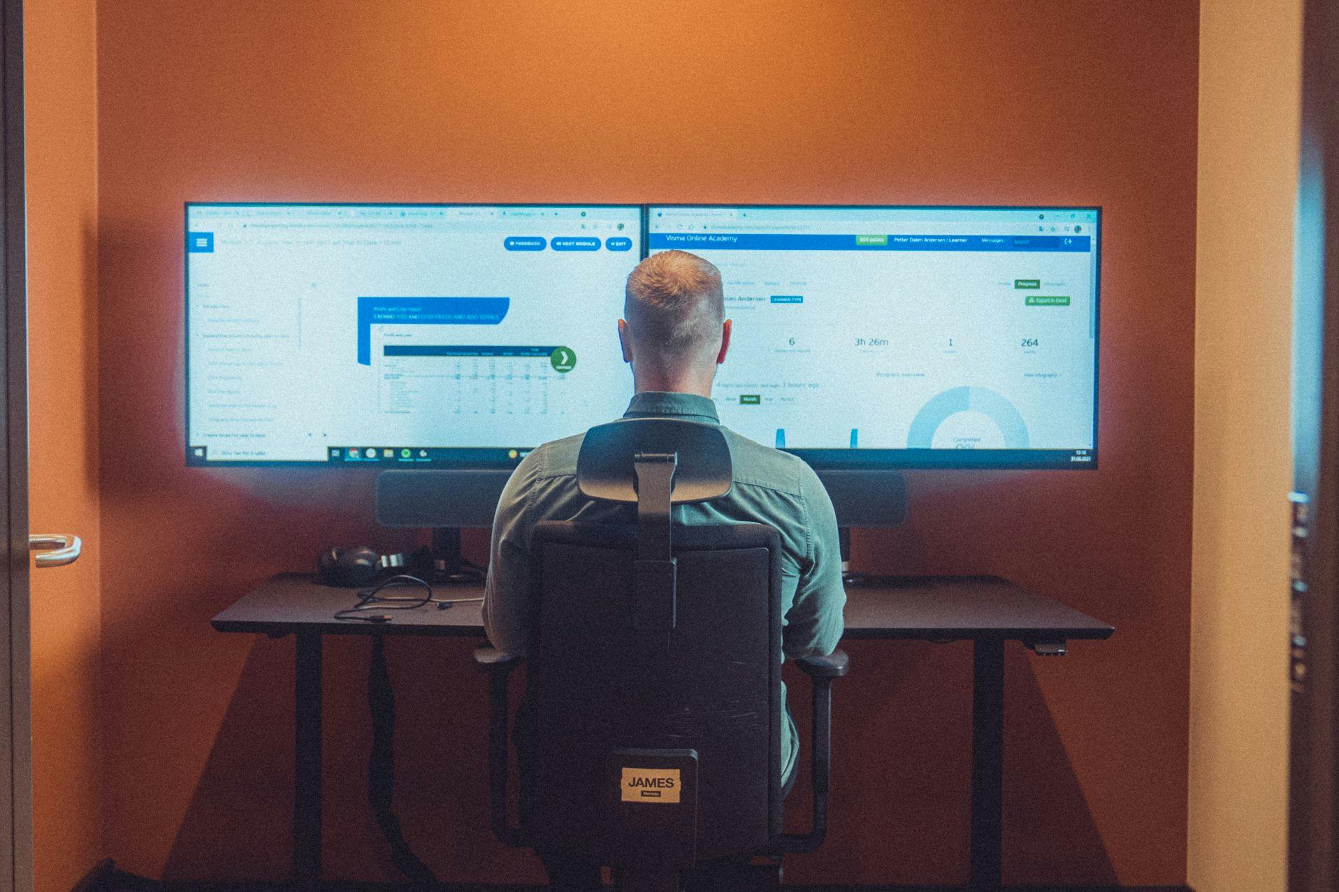 Person som sees bakenfra som jobber med to dataskjermer, inne på Visma.net systemet